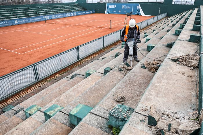 Slika radnika kako pneumatičkim čekićem ruši tribine pored teniskog terena.